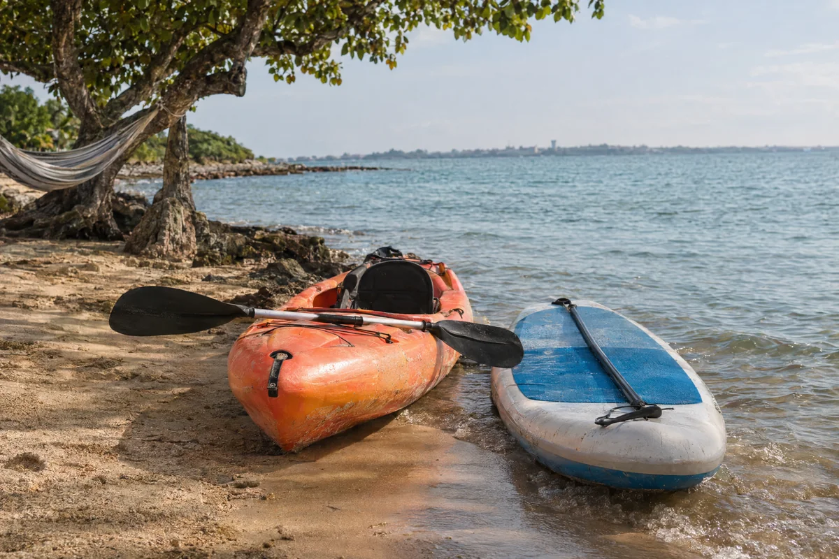 Kayak y tabla de paddle junto a la orilla, con una hamaca al fondo. Imagen ilustrativa.